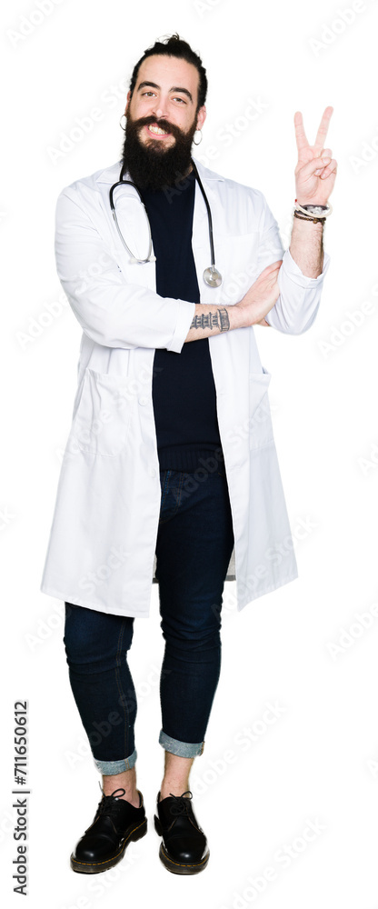 Doctor with long hair wearing medical coat and stethoscope smiling with happy face winking at the camera doing victory sign. Number two. Doctor with long hair wearing medical coat and stethoscope smiling with happy face winking at the camera doing victory sign. Number two.