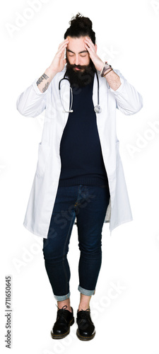 Doctor with long hair wearing medical coat and stethoscope with hand on head for pain in head because stress. Suffering migraine. © Krakenimages.com