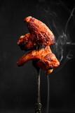 Traditional Buffalo BBQ chicken wings, on a fork. On a black background.