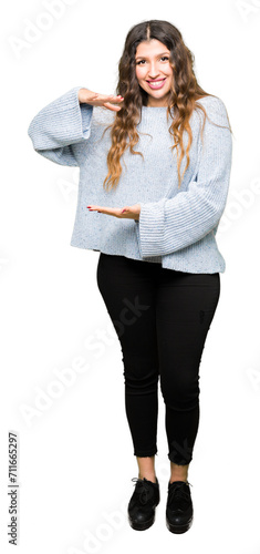 Young beautiful woman wearing winter sweater gesturing with hands showing big and large size sign, measure symbol. Smiling looking at the camera. Measuring concept.