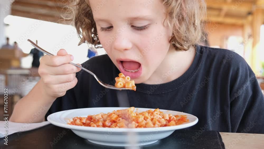 Curly-haired boy eating pasta with tomato sauce in a cafe. Kids food menu. Curly-haired boy eating pasta with tomato sauce in a cafe. Kids food menu.
