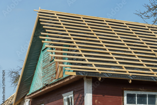 A new wooden roof structure facing an old wooden house in the village. Industrial roofing system with wooden beams, beams and tiles. Roofing works.