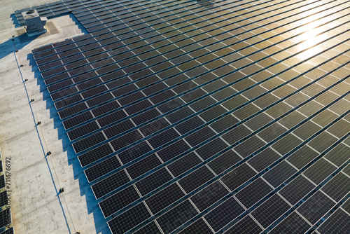 Aerial view of solar power plant with blue photovoltaic panels mounted on industrial building roof for producing green ecological electricity. Production of sustainable energy concept