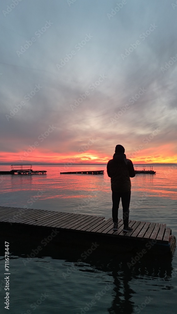 Fototapeta premium uomo guarda il tramonto sul pontile del lago