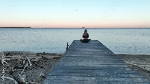The young woman does meditation on the wood pier by the sea. Morning, dawn. Aerial view	
 photo