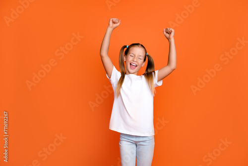 Photo portrait of pretty small girl raise fists celebrate scream lottery dressed stylish white outfit isolated on orange color background photo