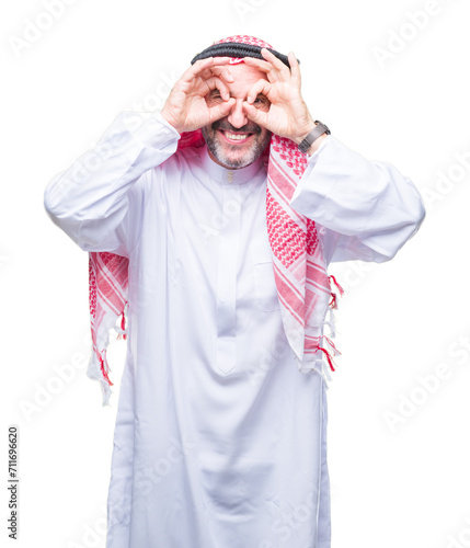 Senior arab man wearing keffiyeh over isolated background doing ok gesture like binoculars sticking tongue out, eyes looking through fingers. Crazy expression.