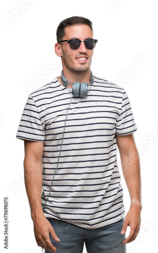 Handsome young man wearing headphones looking away to side with smile on face, natural expression. Laughing confident.