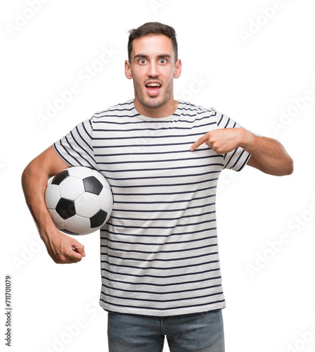 Handsome young man holding soccer football with surprise face pointing finger to himself