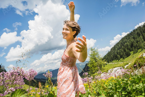 Frau tanzt vor Freude in Blumenwiese in den Bergen, Österreich photo