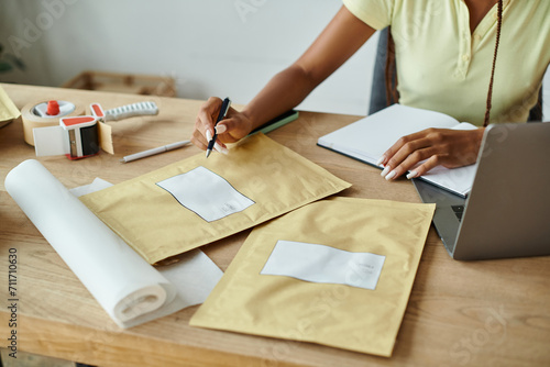 cropped view of young african american female merchant signing post packets, delivery concept