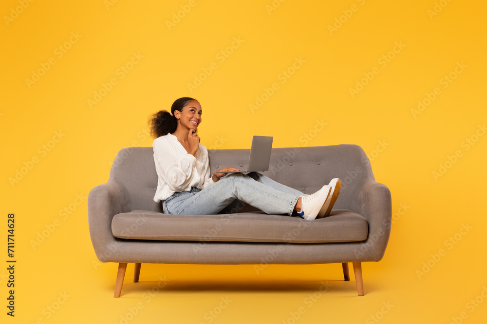 teenager black girl uses laptop on sofa against yellow background