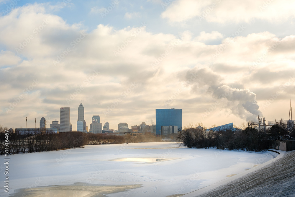 A view of the Indianapolis skyline from White River State Park. The White River is frozen in the foreground with the city in the background. The sky is colorful from the mix of sun, clouds, and sky. A view of the Indianapolis skyline from White River State Park. The White River is frozen in the foreground with the city in the background. The sky is colorful from the mix of sun, clouds, and sky.