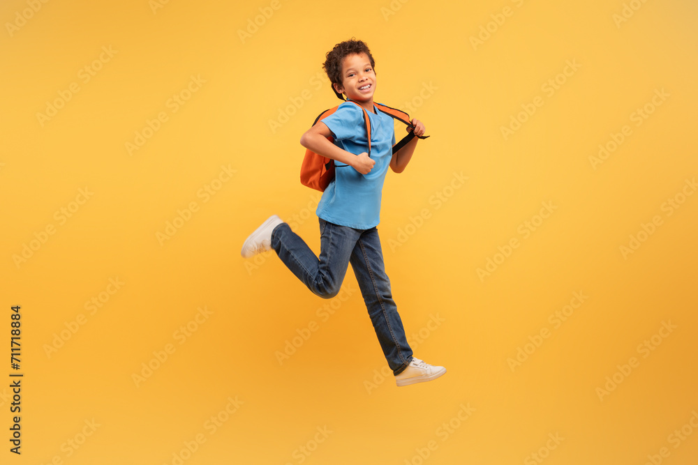 Joyful boy jumping with backpack on vibrant yellow background