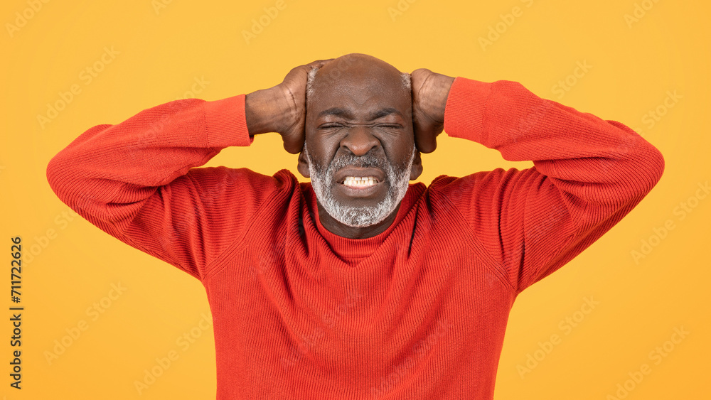 Frustrated senior man in a red sweater and hat, clutching his head with a grimace Frustrated senior man in a red sweater and hat, clutching his head with a grimace