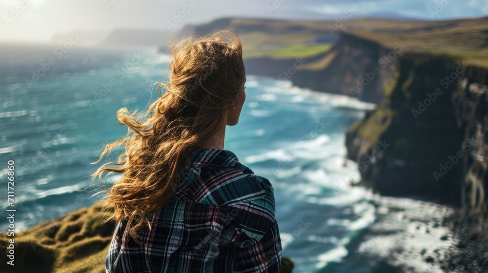 Fototapeta premium Woman standing on a cliff with her hair caught in the breeze generative ai