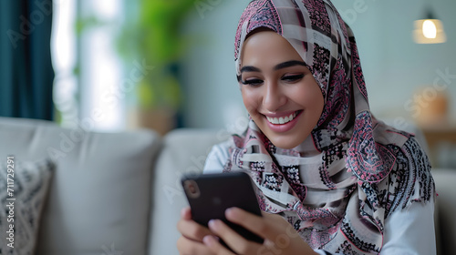 Smiling young beauty muslim woman at home relaxed texting using mobile phone, technology communication concept photo