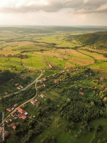 Aerial drone flight above a rural region in Transylvania at sunset. Grassy hills, orchards, agricultural fields, meadows, storm clouds and sunlight create a beautiful countryside landscape. Romania © Alexandru V