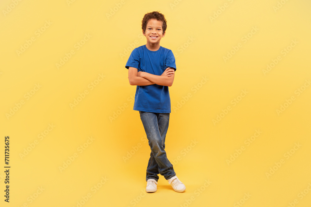 Confident boy with arms crossed in blue shirt on yellow Confident boy with arms crossed in blue shirt on yellow
