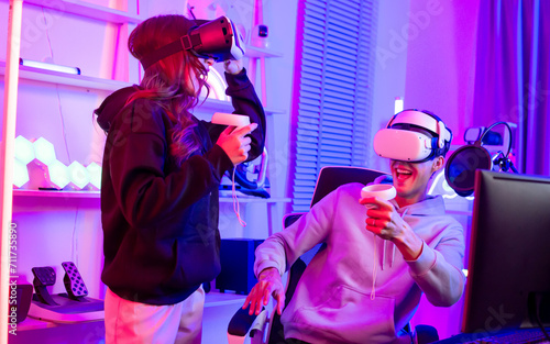Adult couple online game streamer in social media, laughing, wearing VR virtual reality glass to playing with amusement, fun while staying at home with mixed color of neon light. Technology Concept.
