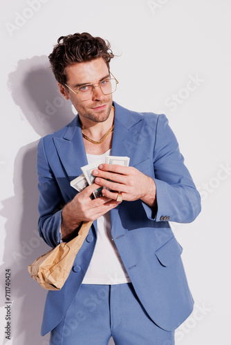Trendy man in suit and tank top holding cash and paper bag on grey, fashion concept  © Dmytro Hai