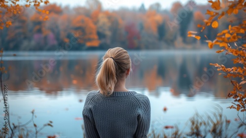 Woman with her back to the camera, looking out over a calm lake surrounded by autumn foliage generative ai