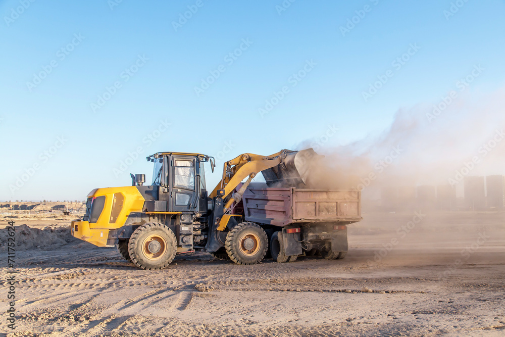 Tractor loader loads a truck on a construction site.Dust on a construction site.Blur.