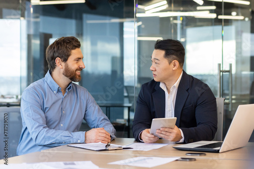 Two professional businessmen collaborating in a modern office setting. Work discussion between colleagues in the corporate world.