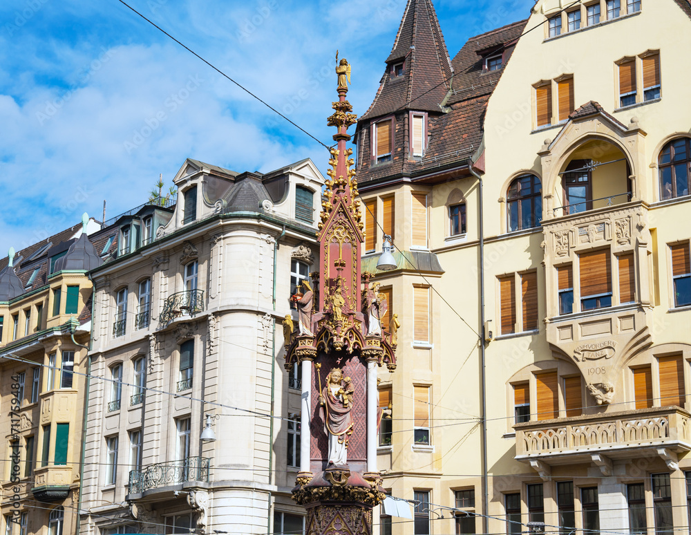 Renaissance era column in the middle of Fischmarkt fairground in Basel with nice Swiss buildings in the background on a sunny day