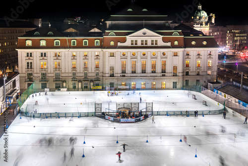 Illuminated ice skating rink in Vienna, Wien, Austria in middle of the historic city center. With many people skating and playing ice hockey in front of palace.