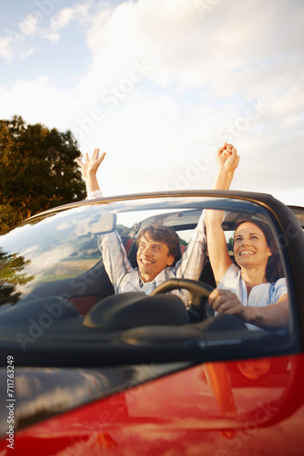 Couple having fun and celebrating while driving in their convertible sports car in the countryside. Munich, Bavaria, Germany