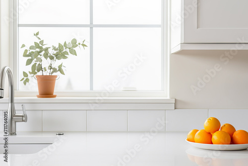 Modern white minimalistic kitchen interior details. Stylish white quartz countertop with kitchen sink with water tap, oranges and potted plant, window and wall cabinet