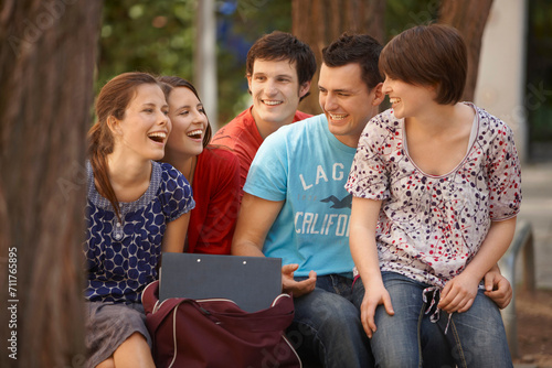 Group of young students sitting together on a bench in a park.