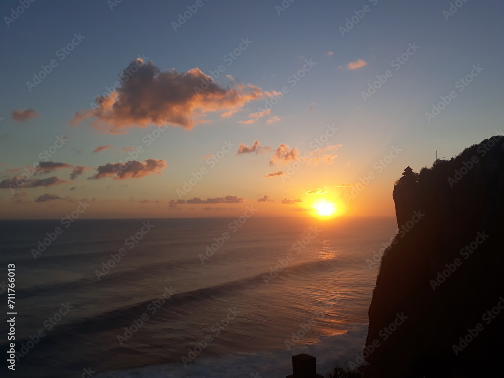 Horizon. The sun sets over the Indian Ocean. Rays illuminate the clouds. Waves, blue clear sky and cliff 