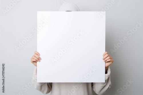 A girl holds a blank white poster and covers her face with it. Generative AI photo