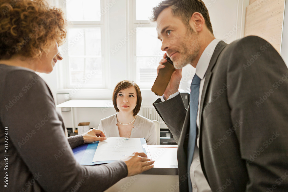 Young business man at a start-up business looking over papers that a female colleague is showing him at the reception desk. Young business man at a start-up business looking over papers that a female colleague is showing him at the reception desk.
