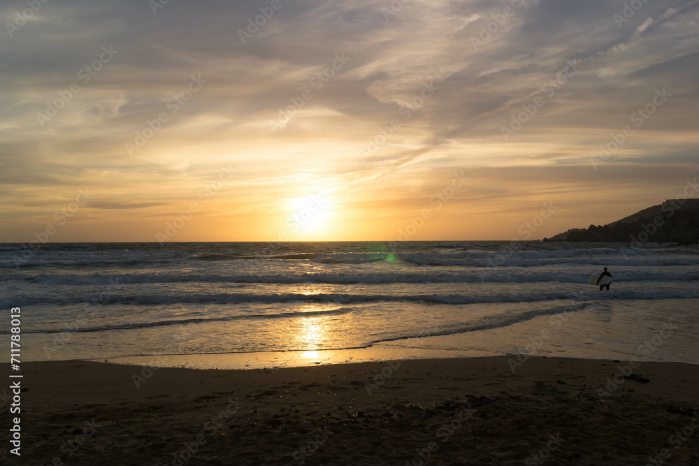 Surfer on the seashore on the beach in Melieha. Sunset in Golden Bay Malta. Surfer on the seashore on the beach in Melieha. Sunset in Golden Bay Malta.