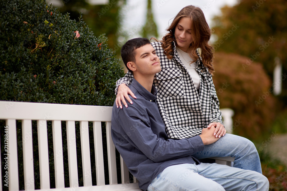 Fototapeta premium Autumn Romance: Young Couple Embracing and Kissing on Park Bench. Young couple kissing and rejoices at the lake. lovely young couple kissing outdoors in autumn. Embraced in Autumn's Warmth: Couple's