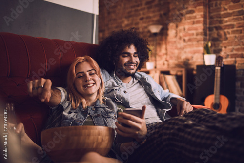 Relaxed couple sharing music on a couch with snacks and drinks photo