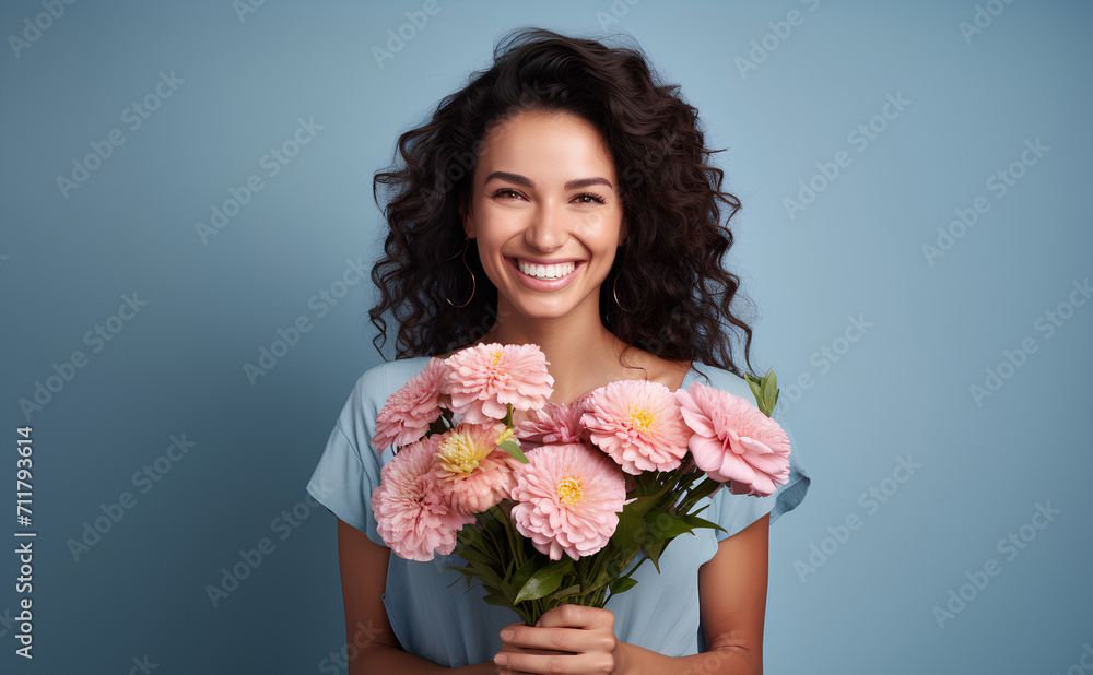 Happy woman with dark hair holding pink spring flowers and smiling on blue background, 8 March, Woman's day, birthday, Mother's day present