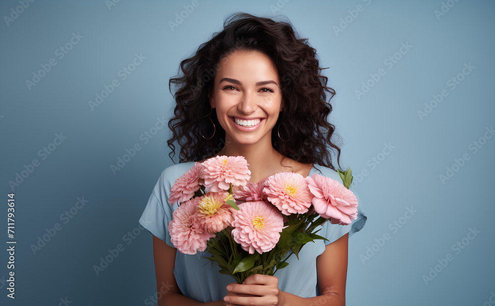 Happy woman with dark hair holding pink spring flowers and smiling on blue background, 8 March, Woman's day, birthday, Mother's day present Happy woman with dark hair holding pink spring flowers and smiling on blue background, 8 March, Woman's day, birthday, Mother's day present