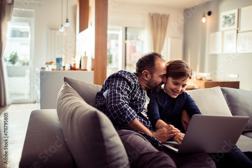 Happy father and son having fun with laptop on the couch