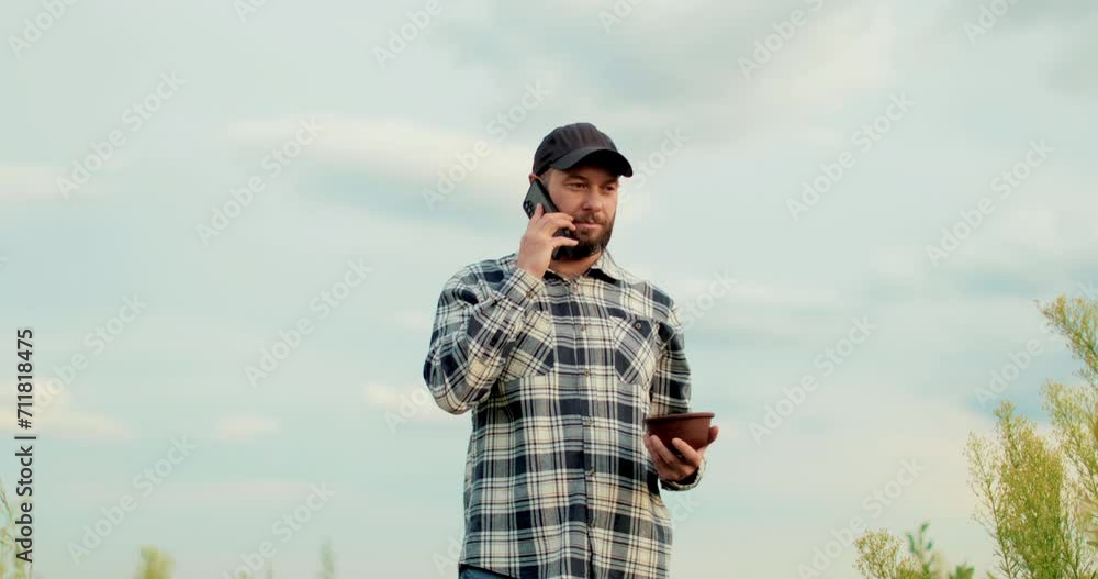 A young farmer is working in a blueberry field, talking on the phone while walking through a blueberry plantation. A young farmer is working in a blueberry field, talking on the phone while walking through a blueberry plantation.