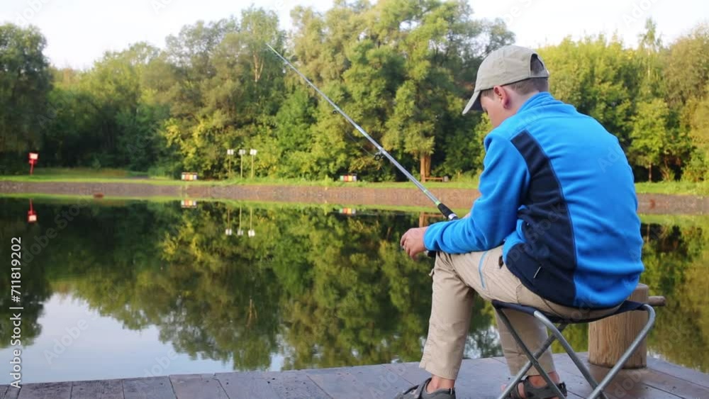 Boy sits near beautiful pond with fishing rod at summer day Boy sits near beautiful pond with fishing rod at summer day