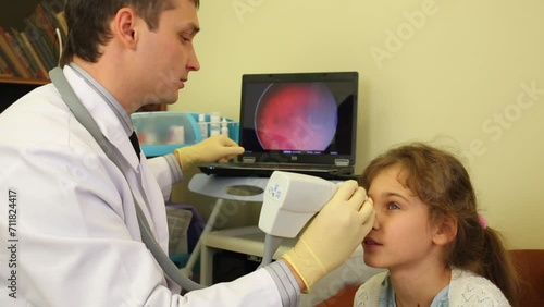 Ophthalmologist inspects girl eye and points at laptop screen photo