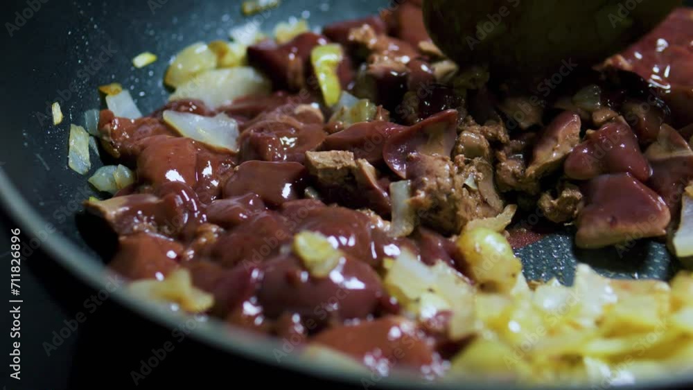 Stirring fried chicken liver with onions in a frying pan with a wooden spatula. Stirring fried chicken liver with onions in a frying pan with a wooden spatula.