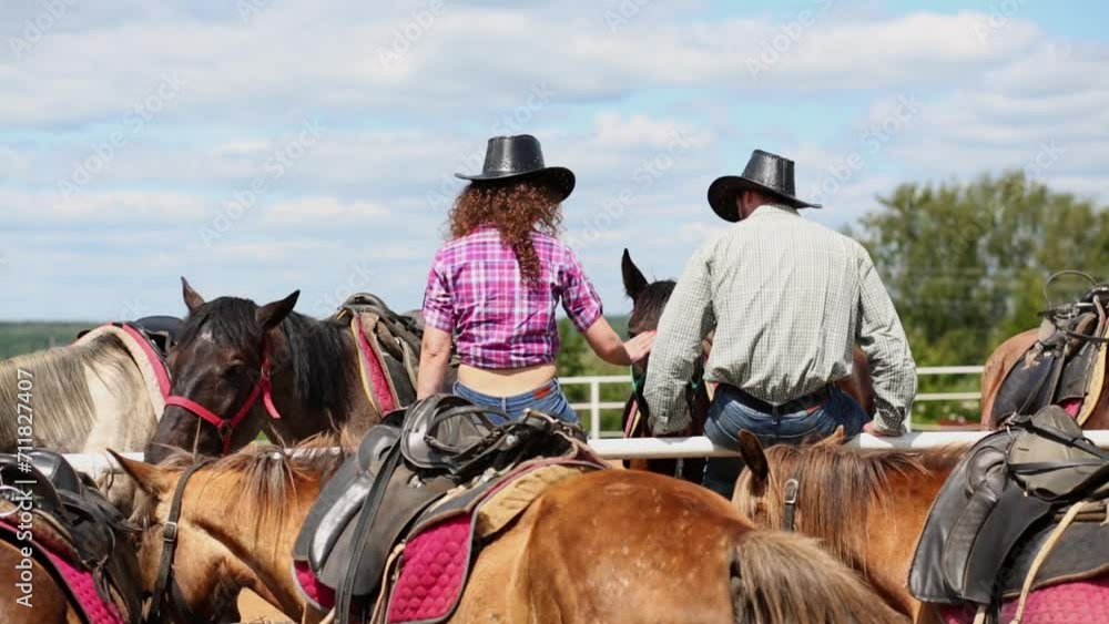 Man and woman sit on metal fence among horses, rear view. Man and woman sit on metal fence among horses, rear view.