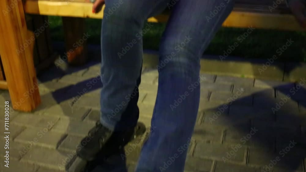 Woman in jeans and roller skates sits on bench in garden at summer Woman in jeans and roller skates sits on bench in garden at summer