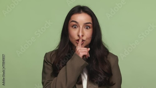 A young Armenian female in a blazer making a shush gesture, signifying secrecy or quiet. The image conveys concepts of privacy and discretion. photo