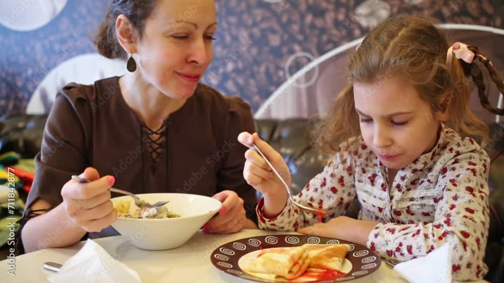 Mother with daughter eating salad and pancakes in cafe Mother with daughter eating salad and pancakes in cafe